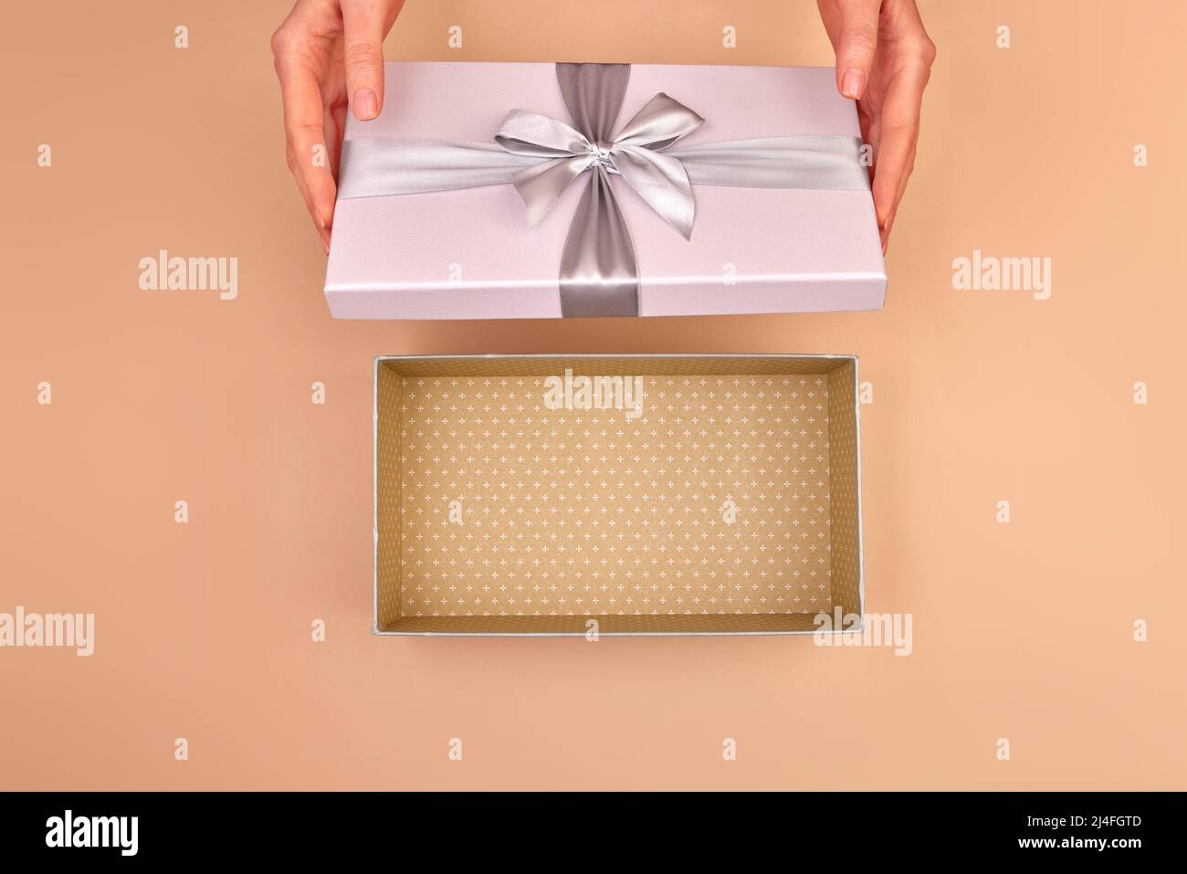 Las manos femeninas abren una caja de luz gris plata con un lazo y puedes ver el paquete vacío beige delicado fondo vista superior Foto de stock