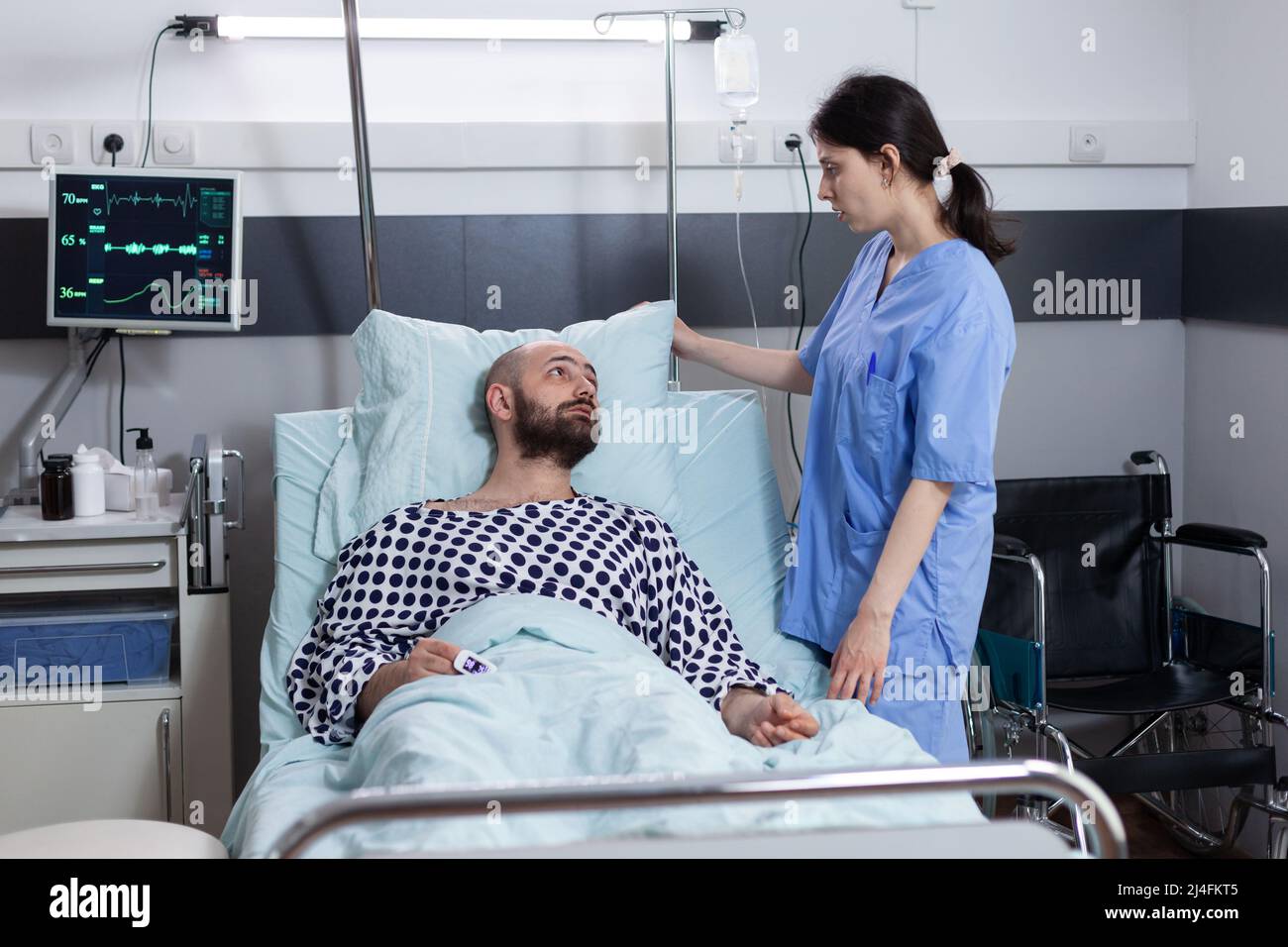 Paciente con insuficiencia respiratoria que pide al cuidador que coloque la almohada mientras está conectado al monitor de signos vitales que muestra una saturación de oxígeno baja. Enfermera cuidando al hombre con problemas respiratorios. Foto de stock