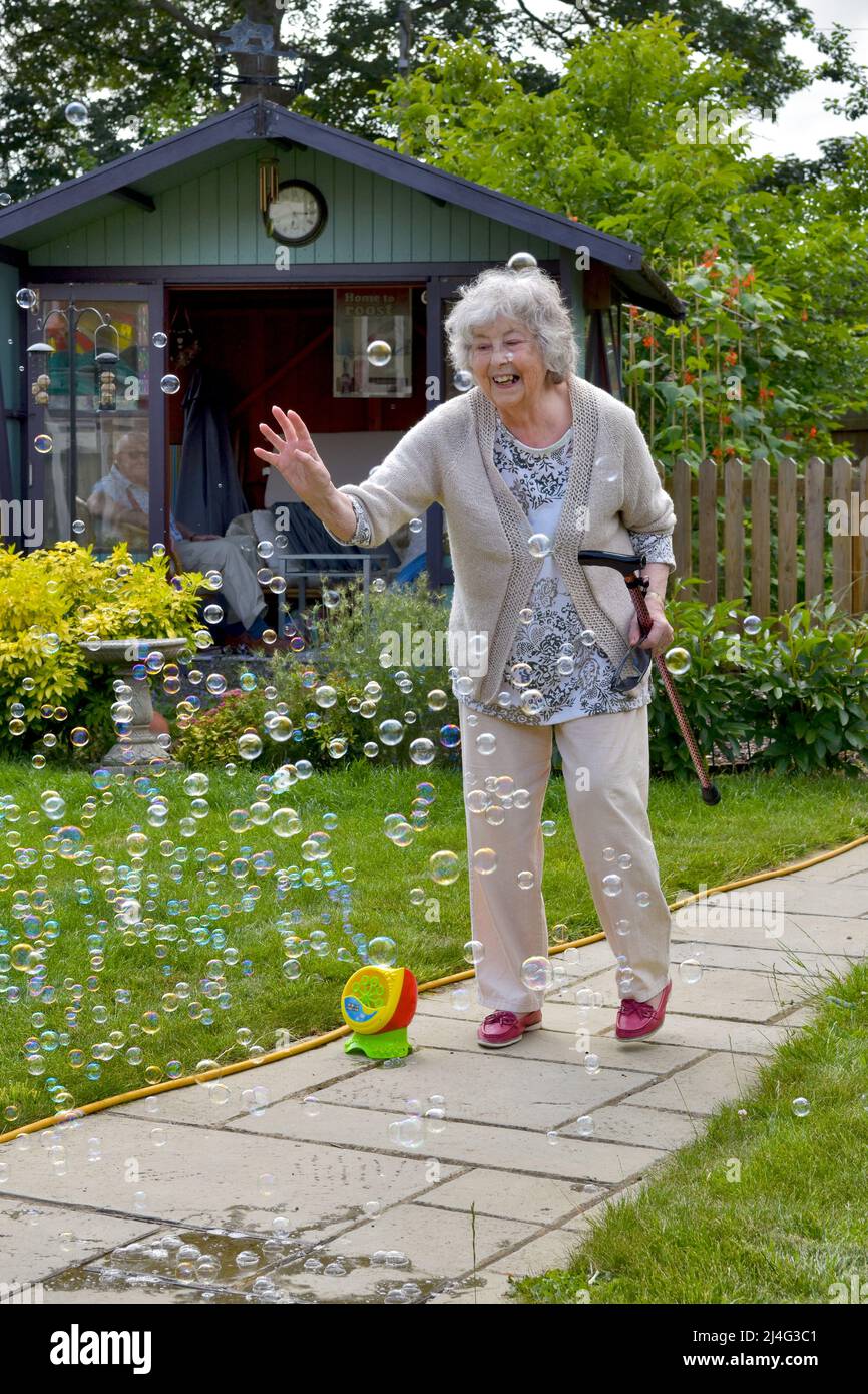 Abuela divertirse con burbujas en el jardín que demuestra que nunca eres demasiado viejo para ser un niño! Concepto de joven de corazón. Foto de stock