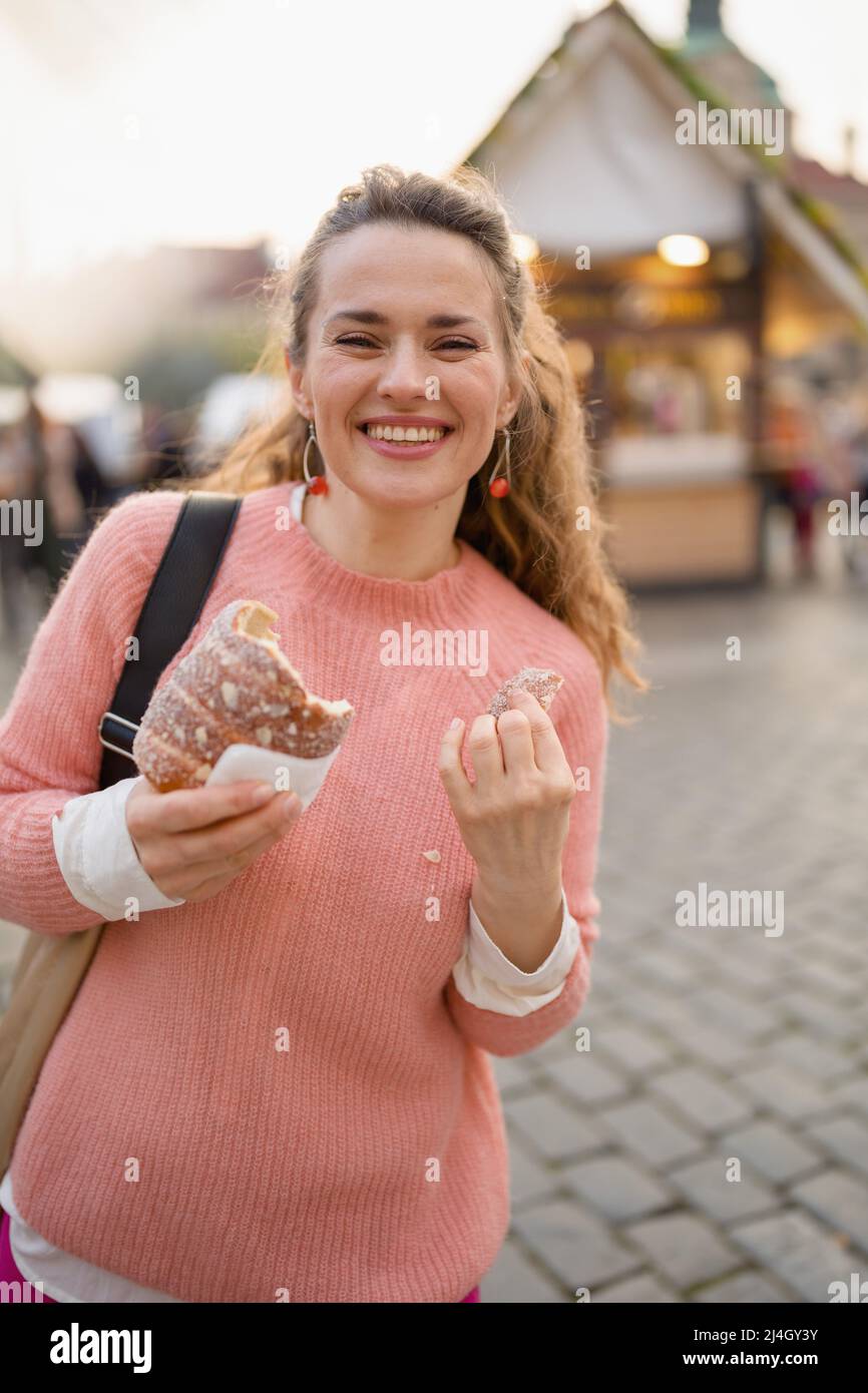 feliz mujer de 40 años en la feria de la ciudad comiendo trdelnik. Foto de stock