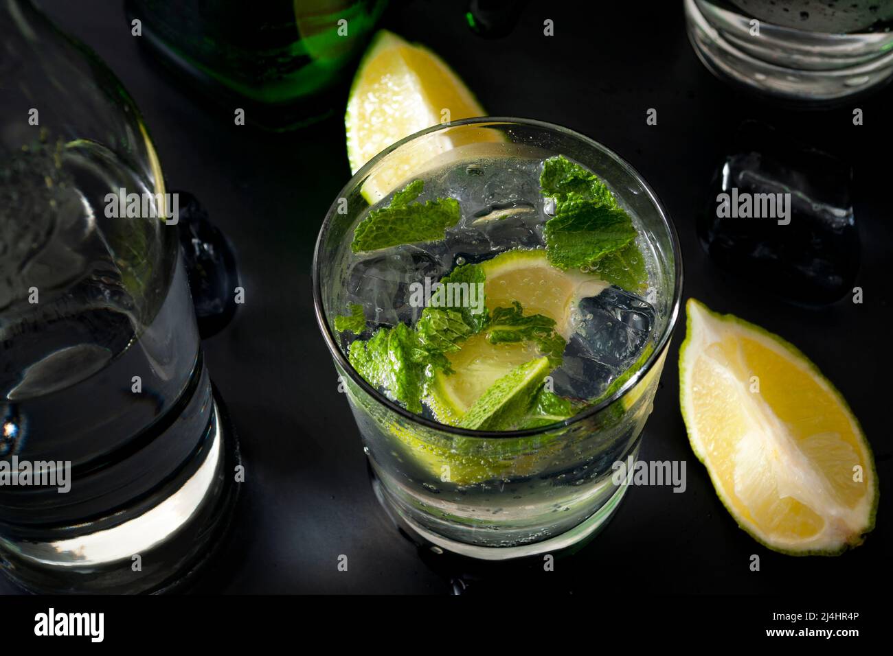 Concepto de cócteles refrescantes y bebidas alcohólicas mixtas con una copa de ginebra y tónica en una barra con una botella de ginebra y agua mineral Foto de stock