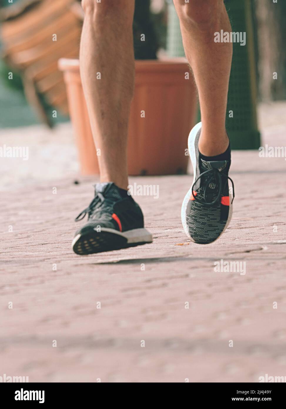 Piernas corriendo en forma de sneakrs. Hombre deportivo de mediana edad runnig por la acera. Correr regularmente al aire libre en el parque. Pavimento rojo duro y piernas en movimiento. Foto de stock