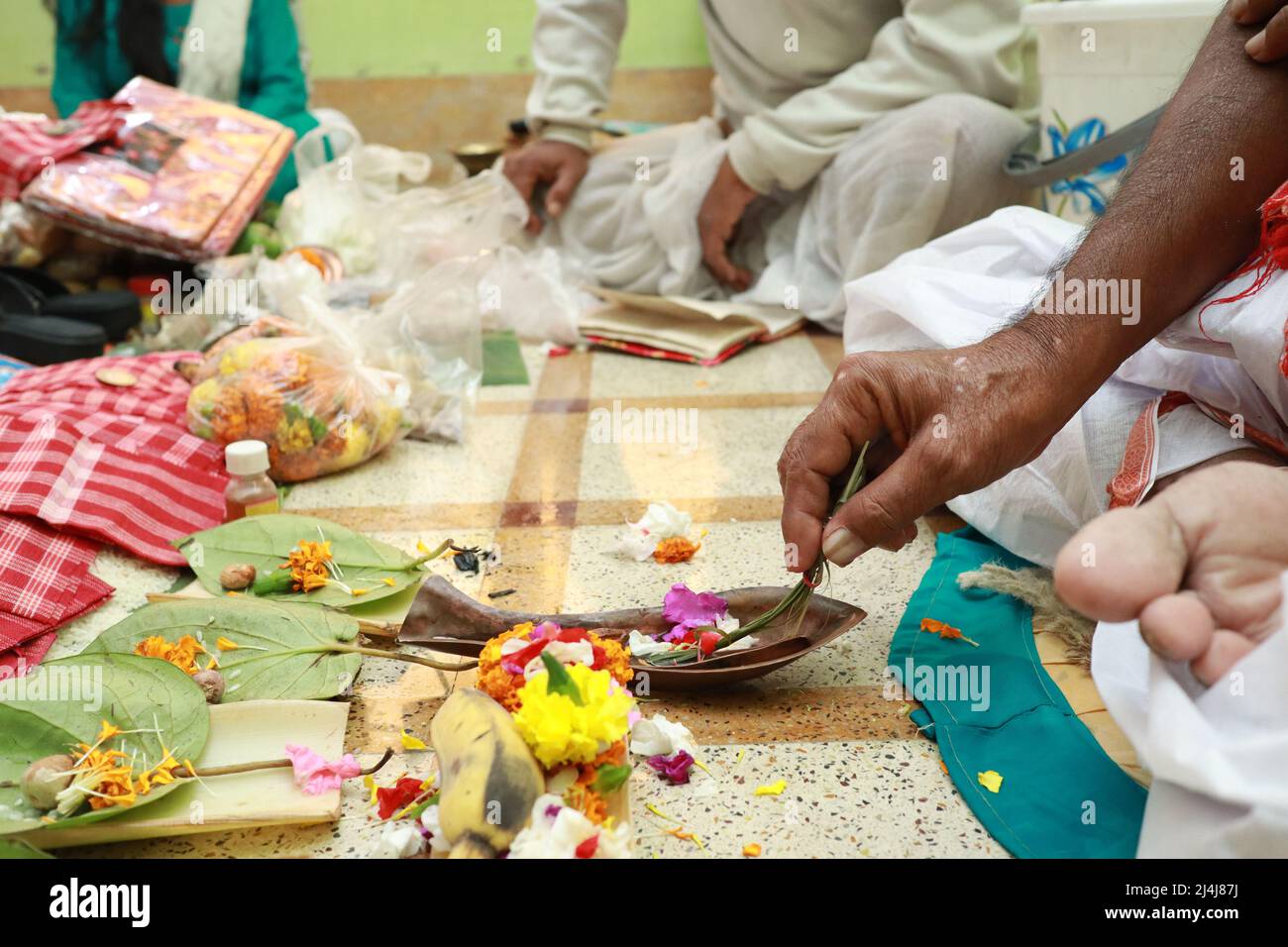 una mano que realiza ritual hindú pooja yajna interior con flores y utensilios de latón. Foto de stock