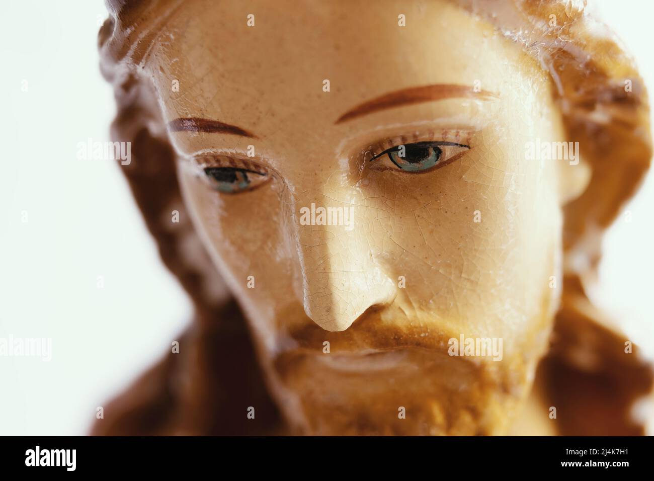 Cara de Jesús mirando hacia abajo, de cerca. Retrato de una pequeña estatua de Jesucristo o figurilla hecha de porcelana o arcilla con rasgos pintados. Foto de stock
