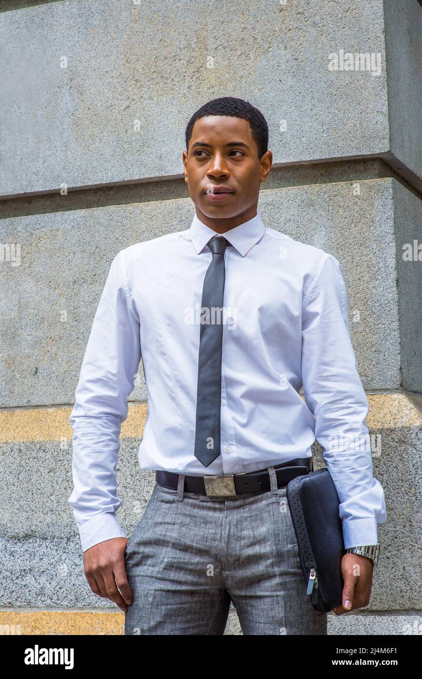 Vestirse en camisa blanca, una corbata negra, pantalones grises, llevar maletín, un joven estudiante universitario negro guapo está parado por una pared piedra, confidentl Fotografía de - Alamy