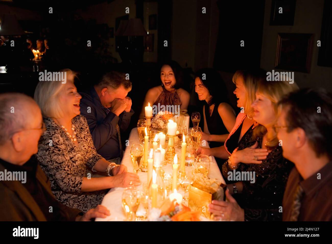 Grupo de amigos riendo mientras un amigo cuenta una historia durante la cena a la luz de las velas Foto de stock