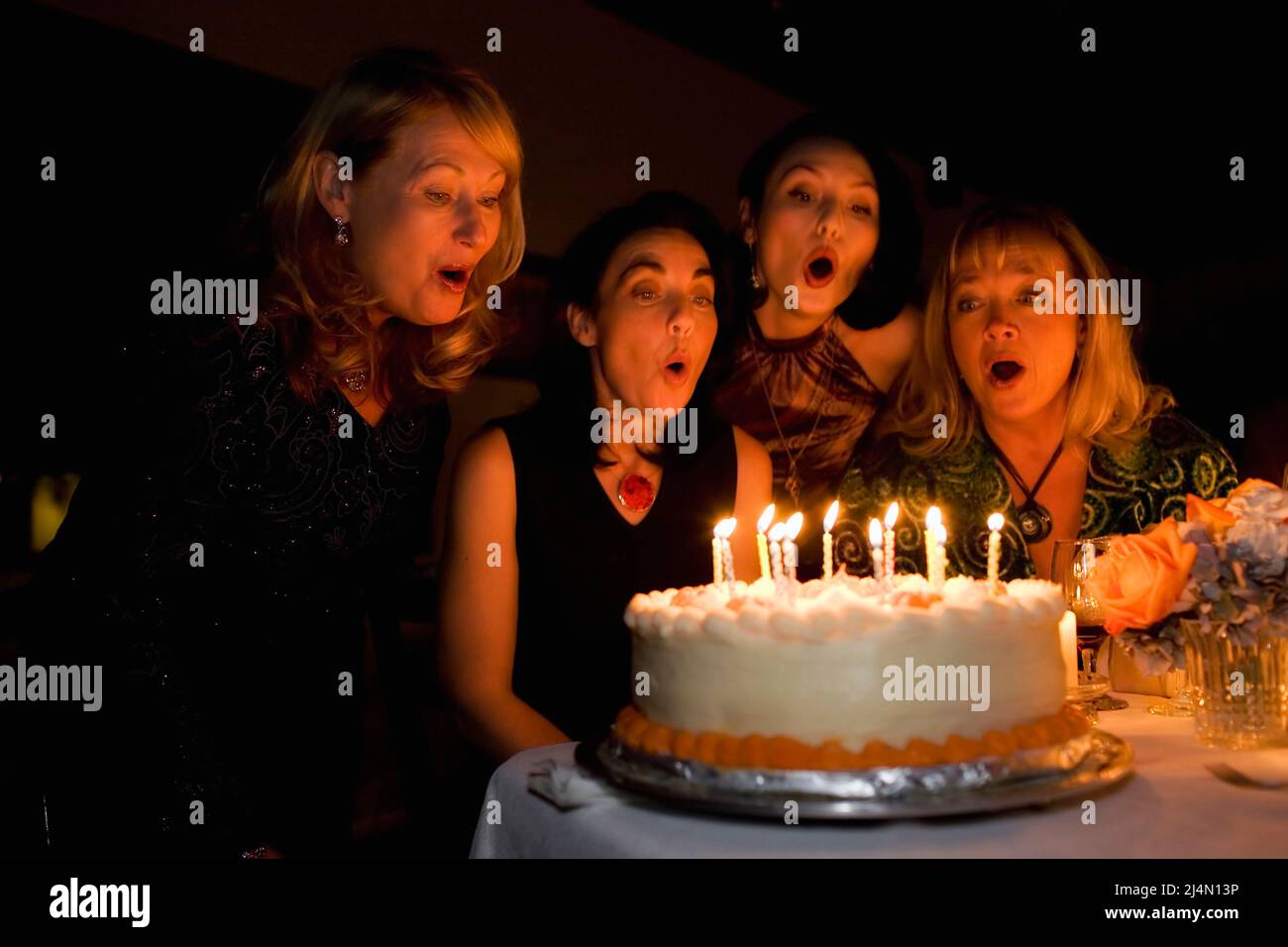 Mujer joven y tres amigos soplando velas en pastel de cumpleaños en la cena Foto de stock