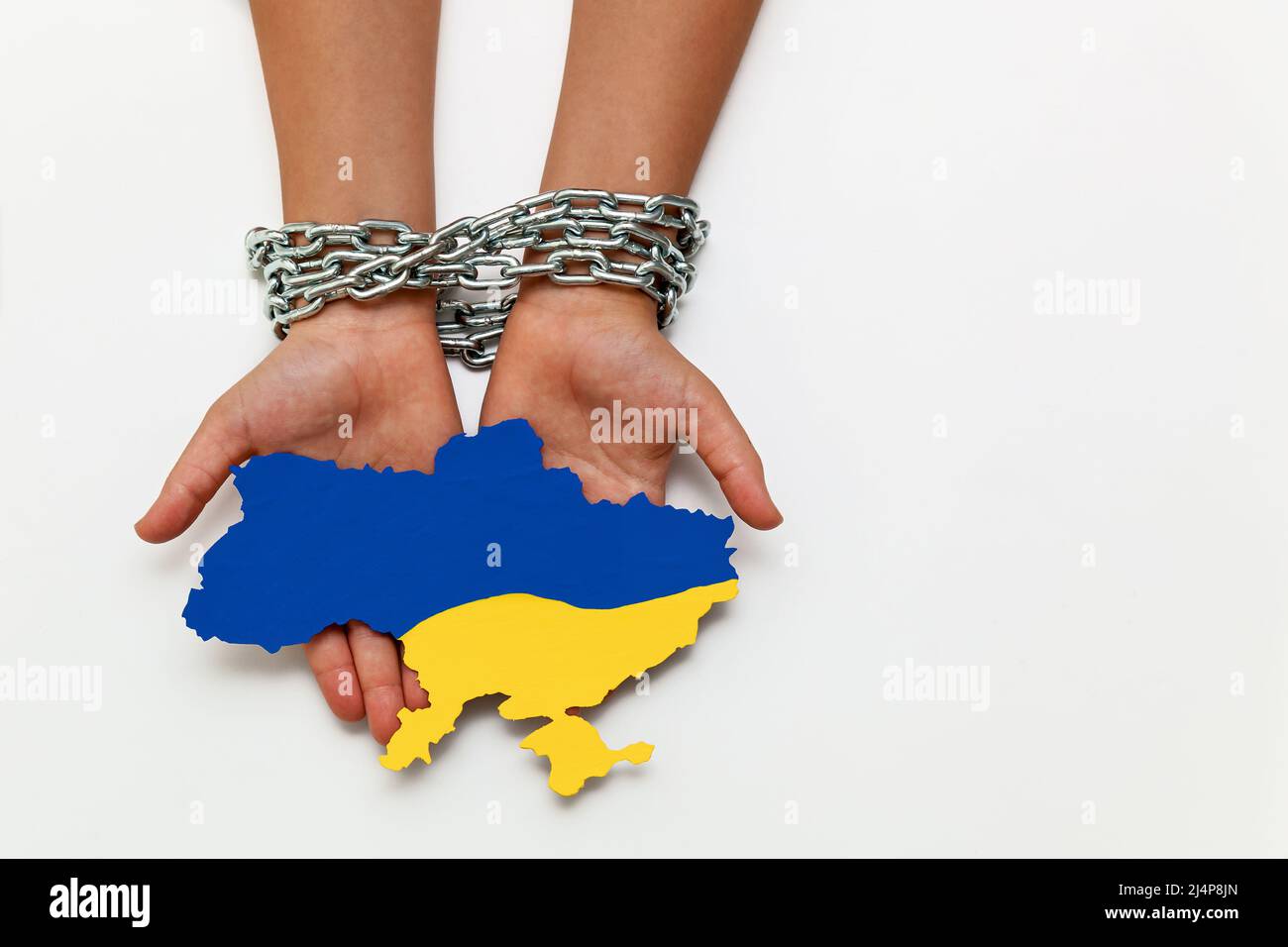 Las manos de las mujeres están atadas con una cadena y sostienen un mapa de Ucrania pintado de azul y amarillo sobre un fondo blanco. Quitar la libertad y la independencia. Foto de stock