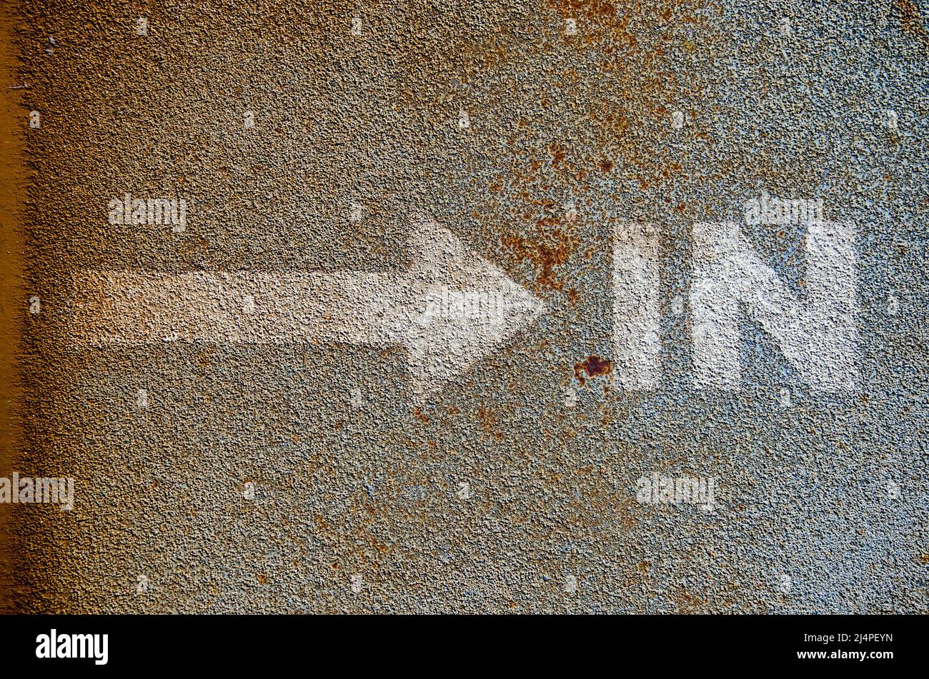 Flecha y la palabra 'in' pintada en blanco en la capa superior de asfalto de un pontón de acero Foto de stock