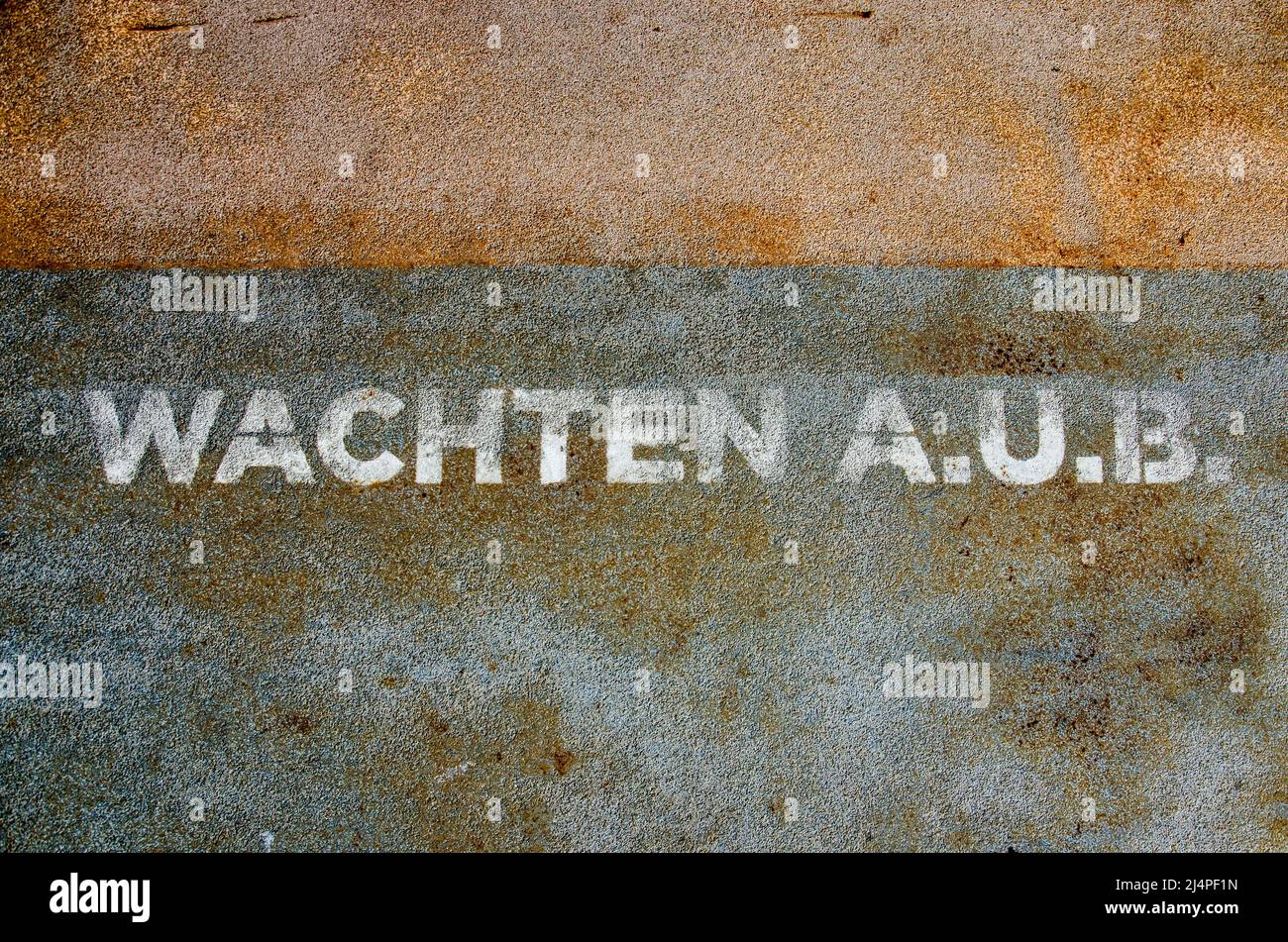 Las palabras holandesas 'wachten a. `b' (por favor espere) escritas en blanco sobre una capa superior rugosa de un pontón de acero Foto de stock