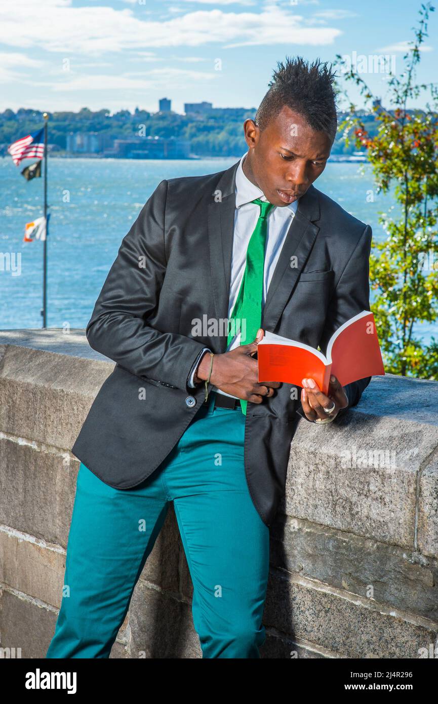 Hombre joven leyendo afuera. Vestirse en una camiseta blanca, un blazer  negro, pantalones verdes, una corbata verde, sosteniendo un libro rojo, un  joven negro con mohaw Fotografía de stock - Alamy