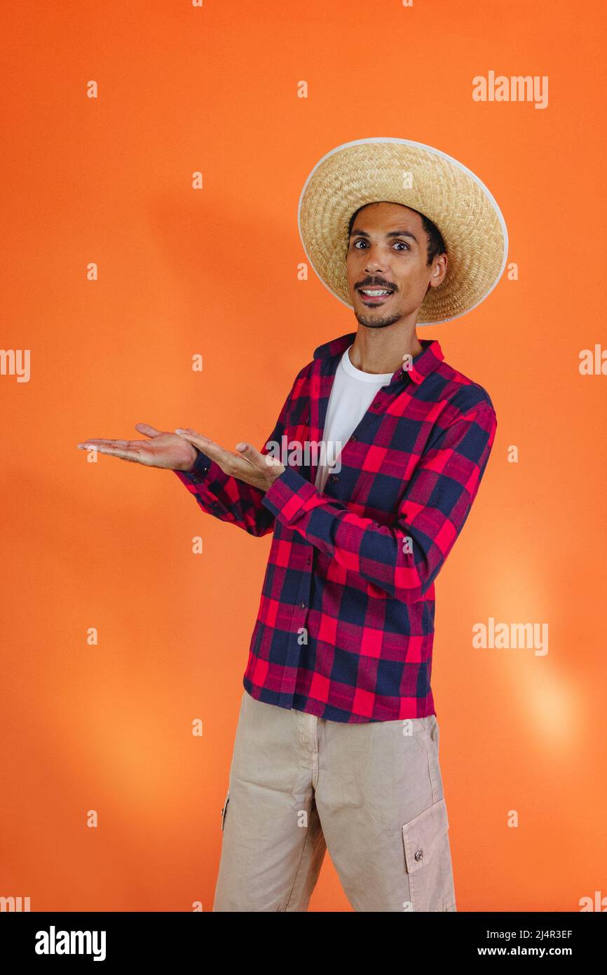 Fiesta Junina. Hombre negro con que apunta aislado sobre fondo naranja. Hombre joven con ropa tradicional para la Festa Junina Fotografía de stock - Alamy