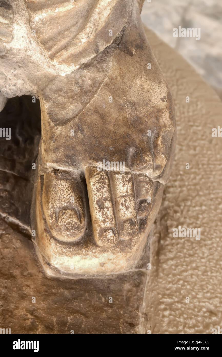 Primer plano del pie en sandalia con los dedos de los pies mostrando la estatua griega antigua - mármol granulado tallado contra un fondo más borroso Foto de stock