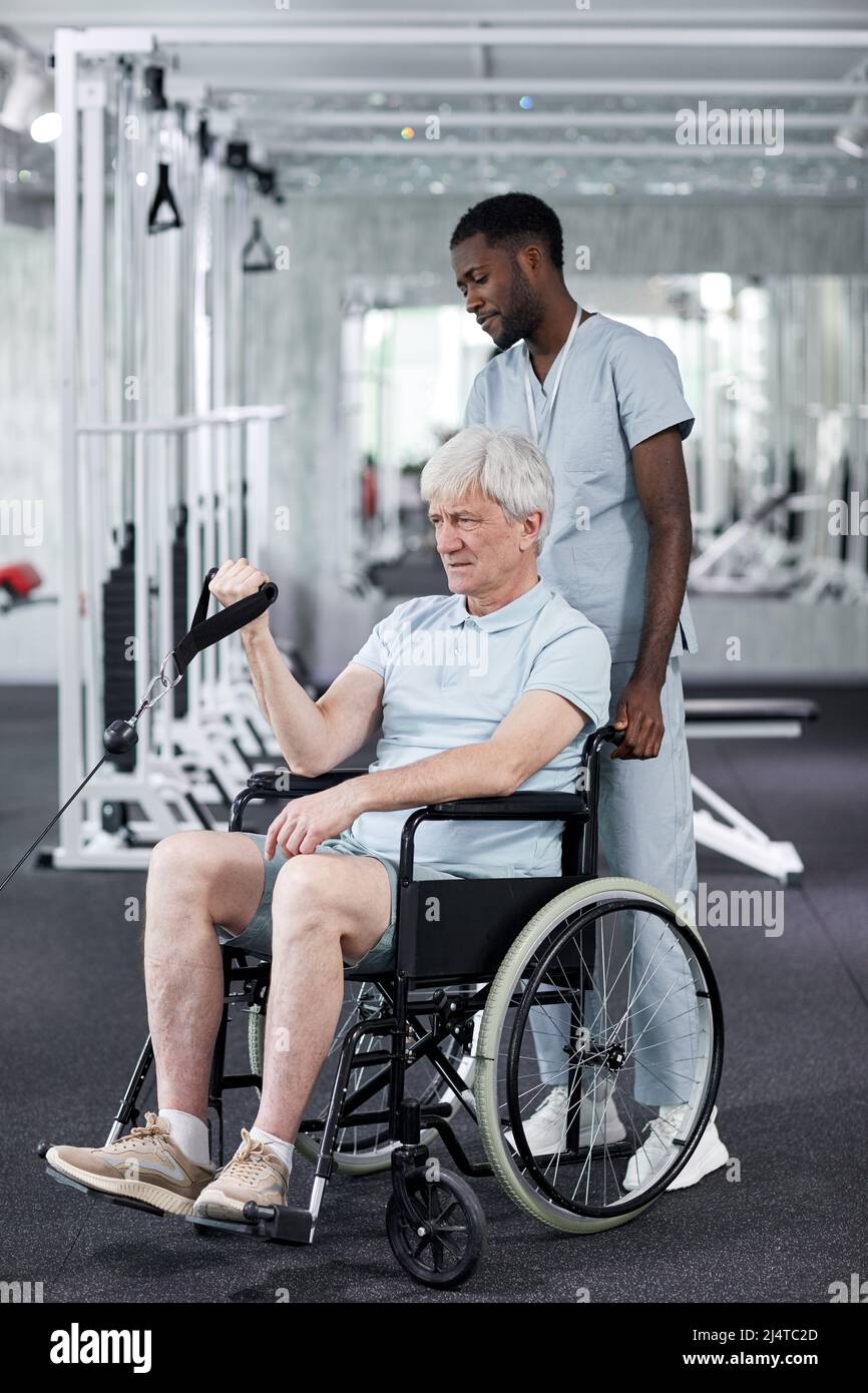 Retrato completo del anciano en silla de ruedas en el gimnasio durante la terapia de rehabilitación en la clínica Foto de stock