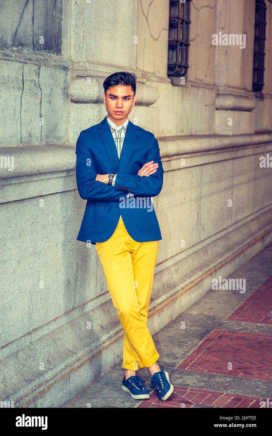 Hombre relajándose afuera. en blazer azul, pantalones amarillos, sneakers, reloj de pulsera, un joven guapo está pie por la pared de estilo de la vieja moda, crossina Fotografía de stock -