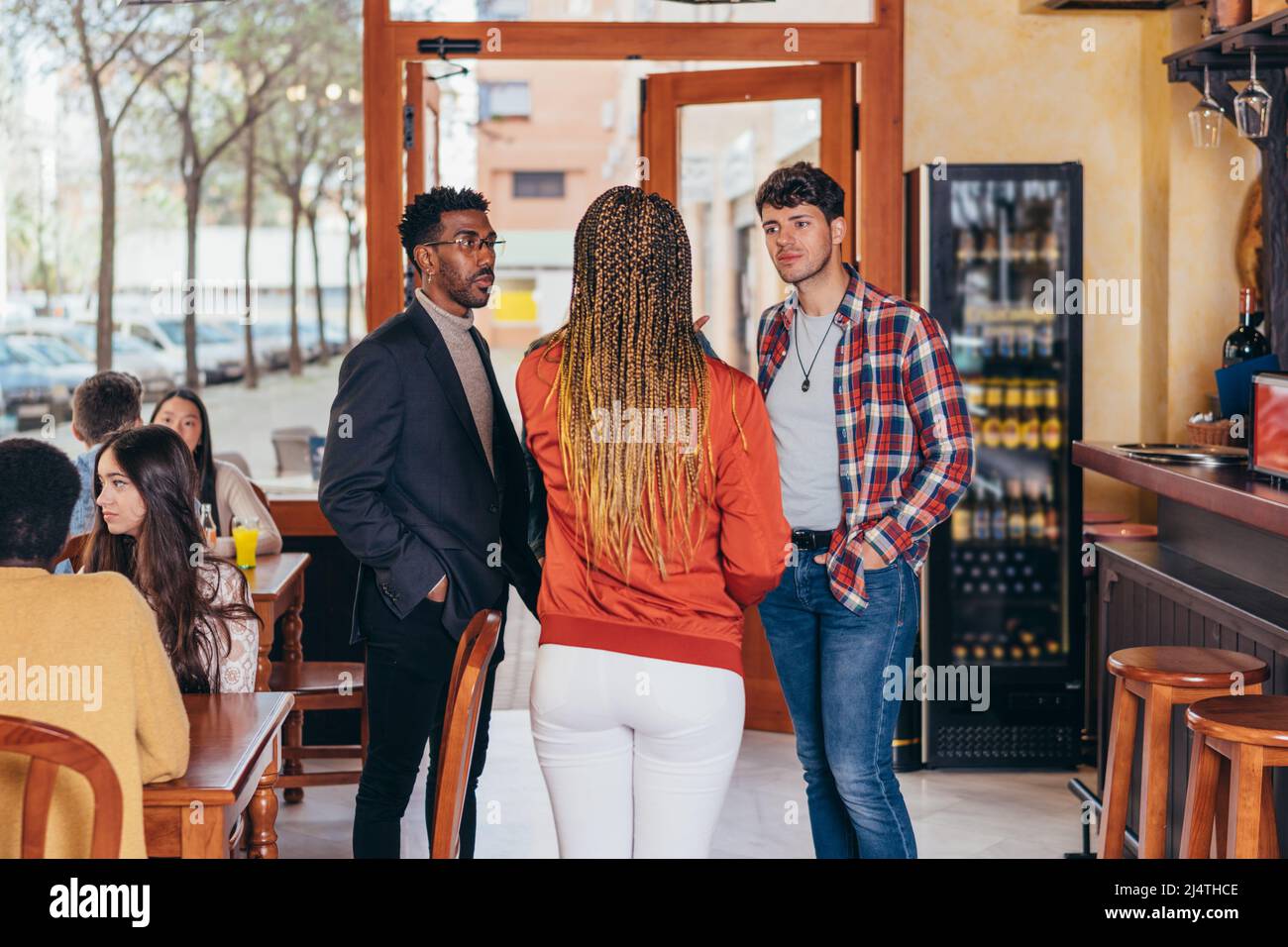 3 personas de diferentes etnias conversan dentro de un bar Foto de stock