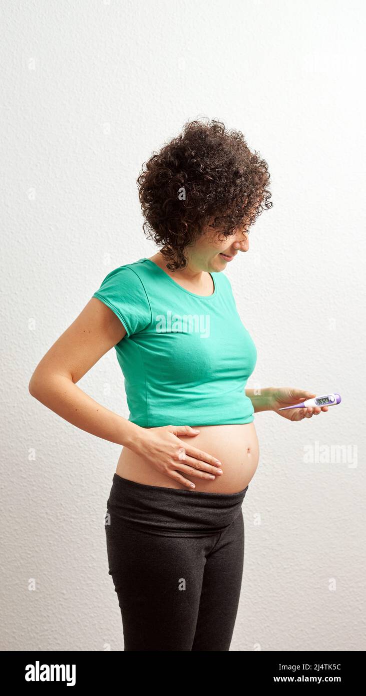 Mujer embarazada con termómetro basal delante de fondo blanco Foto de stock