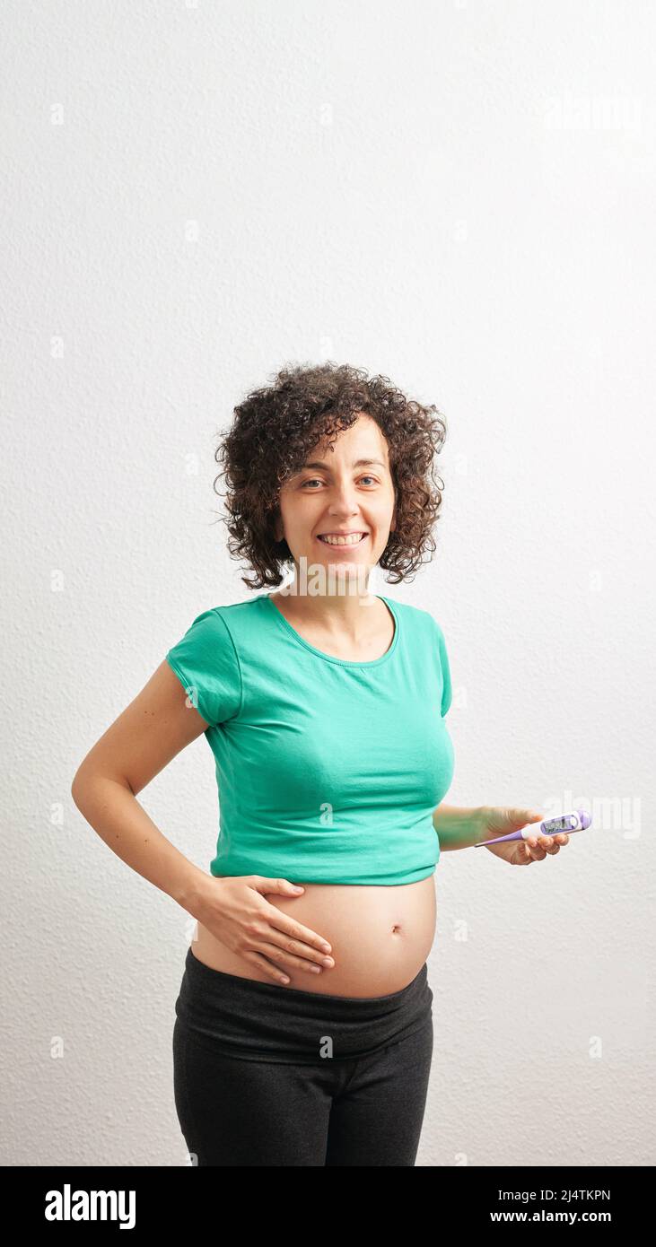 Mujer embarazada con termómetro basal delante de fondo blanco Foto de stock