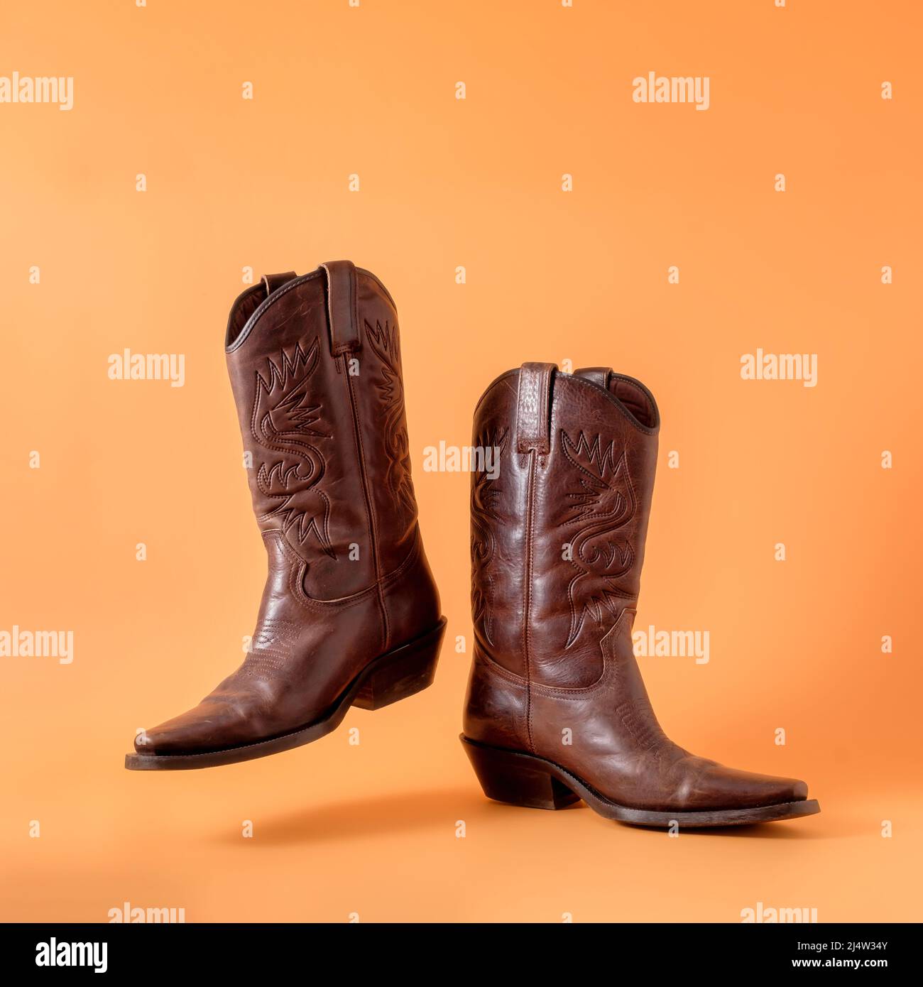 Dos elegantes botas de vaquero clásicas sobre fondo de arcilla naranja. Concepto de vaquero de guardaparques en un rancho en estados unidos texas. Foto de stock