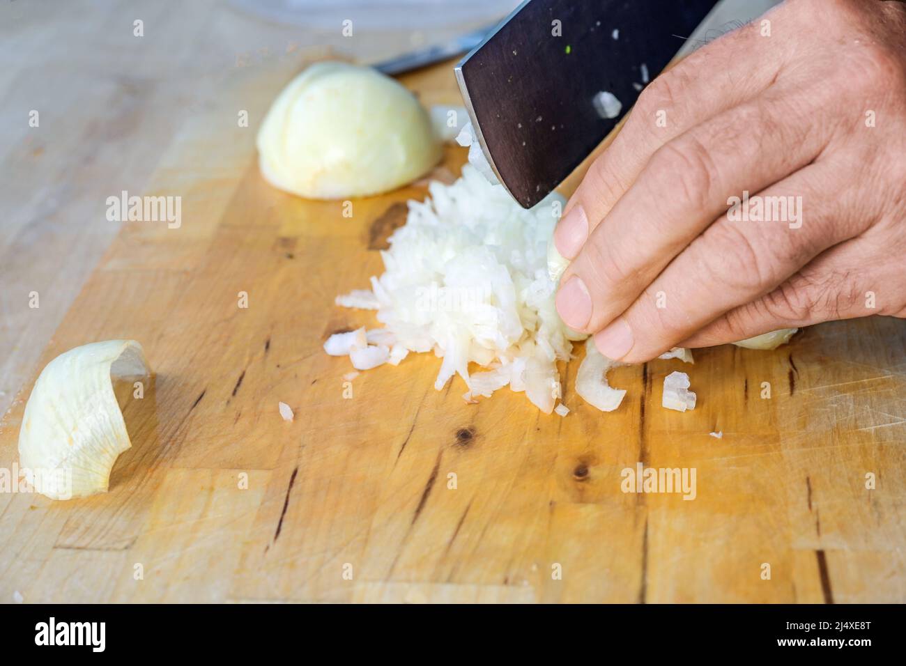 Mano de un hombre cortando cebollas en cubos pequeños con un cuchillo de cocina en una tabla de corte de madera, espacio de copia, foco seleccionado, profundidad de campo estrecha Foto de stock