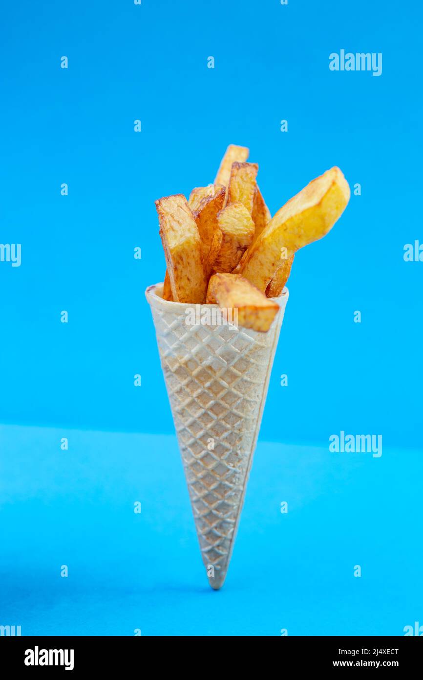 Bouquet de patatas fritas en un cono de helado sobre fondo azul. Comida rápida, concepto de comida callejera. Foto de stock