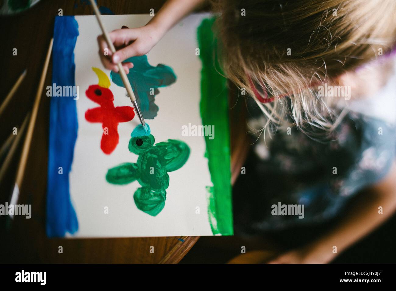 Rubia niña pinta pájaros con colores primarios Foto de stock