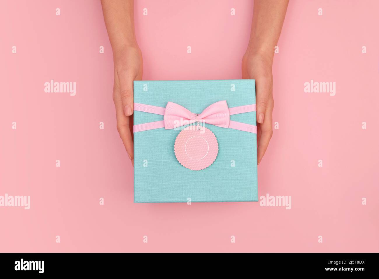 Las manos dan una caja de regalo turquesa con una tarjeta y un lazo en el fondo rosa pastel aislado vista superior Foto de stock