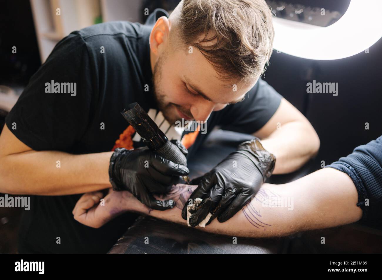 El maestro del tatuaje está tatuando la mano de un hombre. Máquina de tatuaje  inalámbrica, seguridad e higiene en el trabajo. Primer plano del trabajo de  tatuaje. Salón de tatuajes Fotografía de
