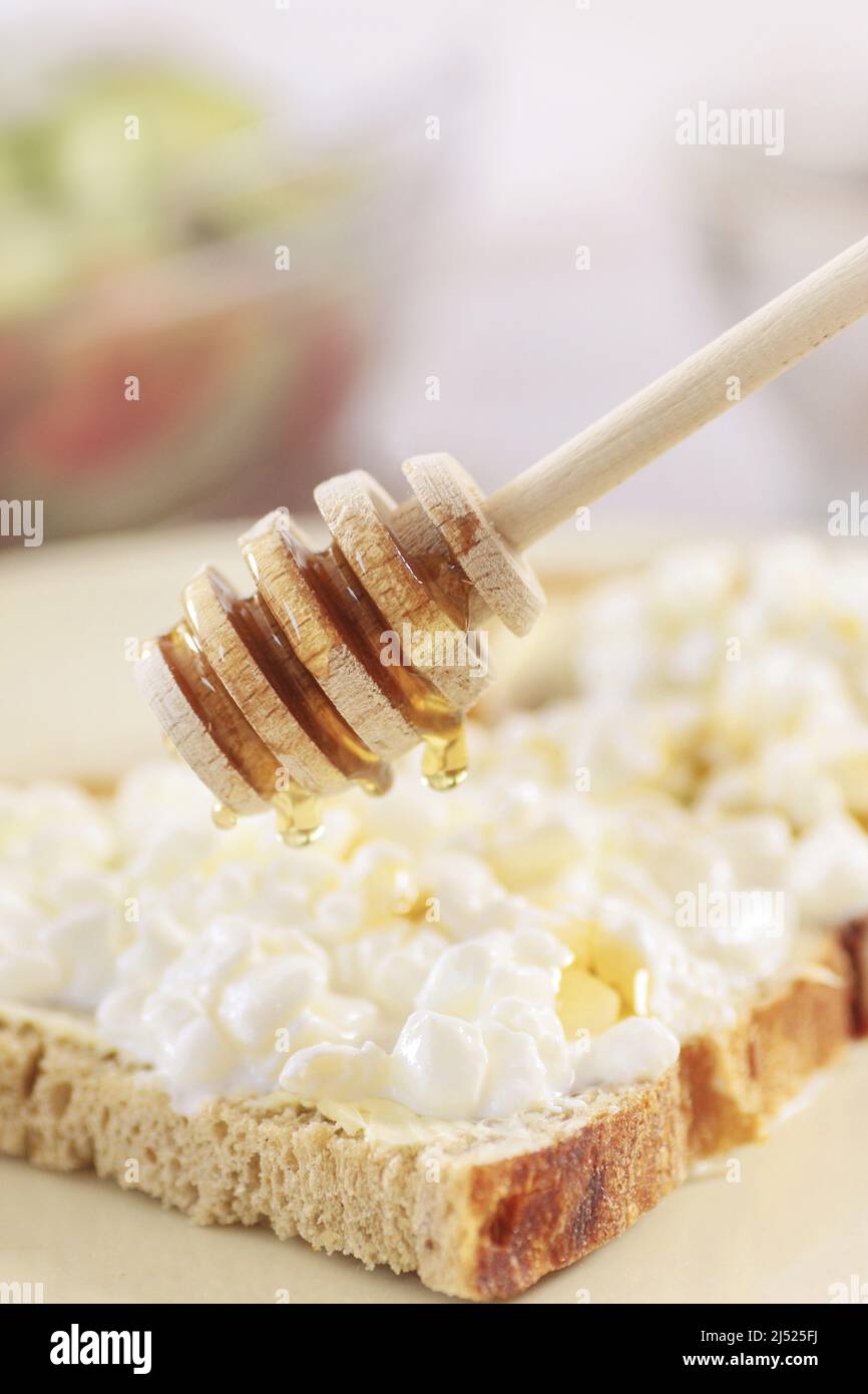 Cuchara de miel sobre la rebanada de pan con queso de casa. Alimentos saludables Foto de stock