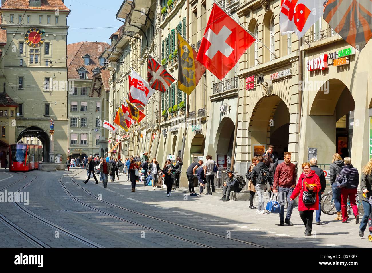 Berna, Suiza - 20 de abril de 2017: Tráfico en una ciudad con muchos peatones y un tranvía que se acerca a distancia. La calle está decorada con fl Foto de stock