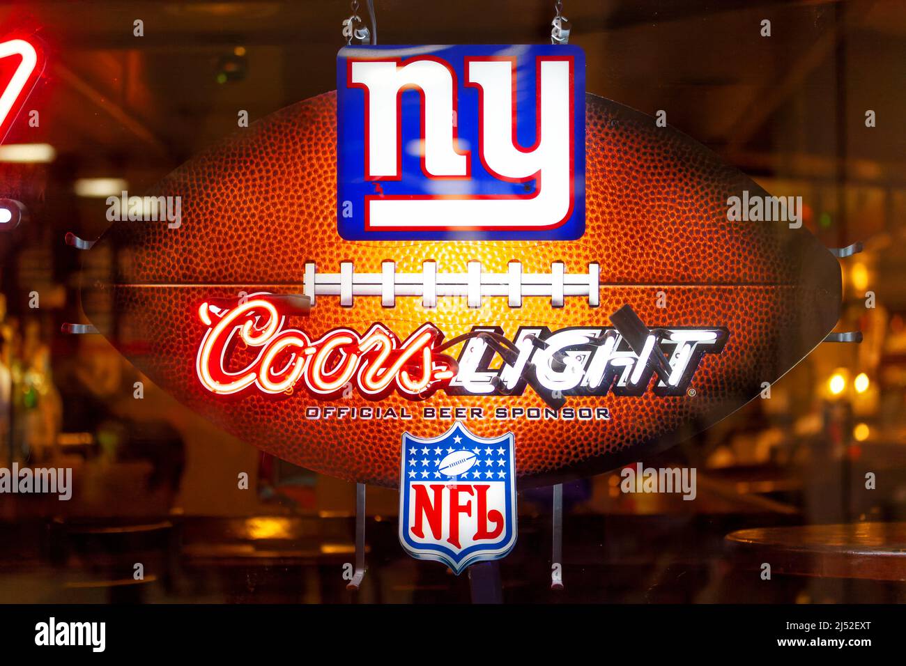 Un signo iluminado de color neón Coors en una ventana de bar. El cartel muestra el logotipo de NY y el logotipo oficial de la NFL. El texto se escribe sobre un fútbol Foto de stock