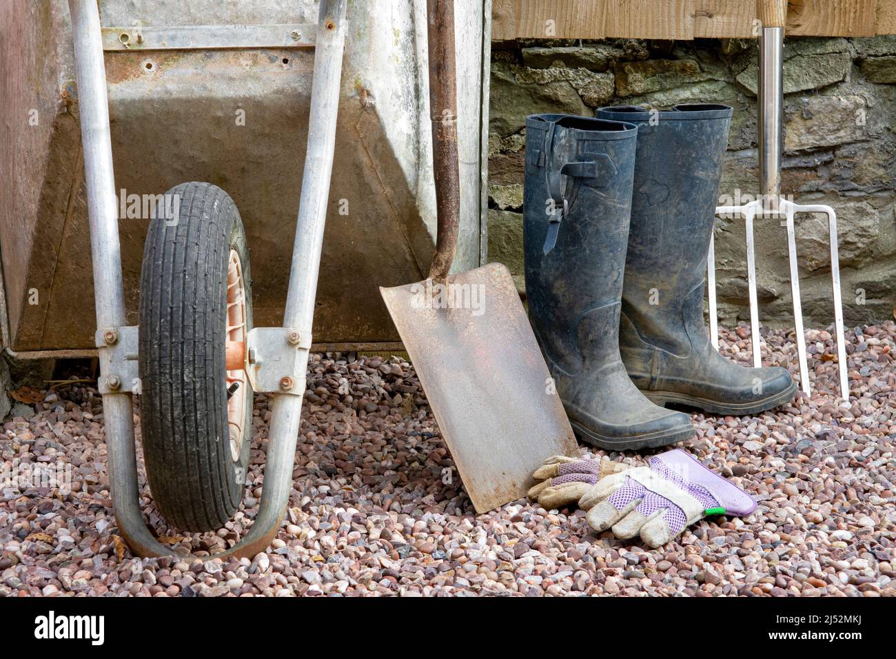 Artículos de jardinería incluyendo carretilla, pala grande, tenedor grande, guantes y botas de agua Foto de stock