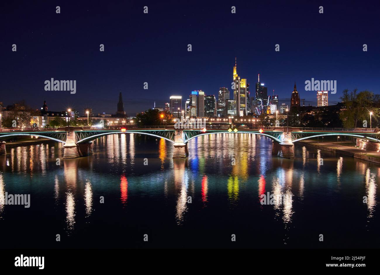El horizonte de Frankfurt y el puente Ignatz Bubis iluminado se reflejan en el río Main por la noche Foto de stock
