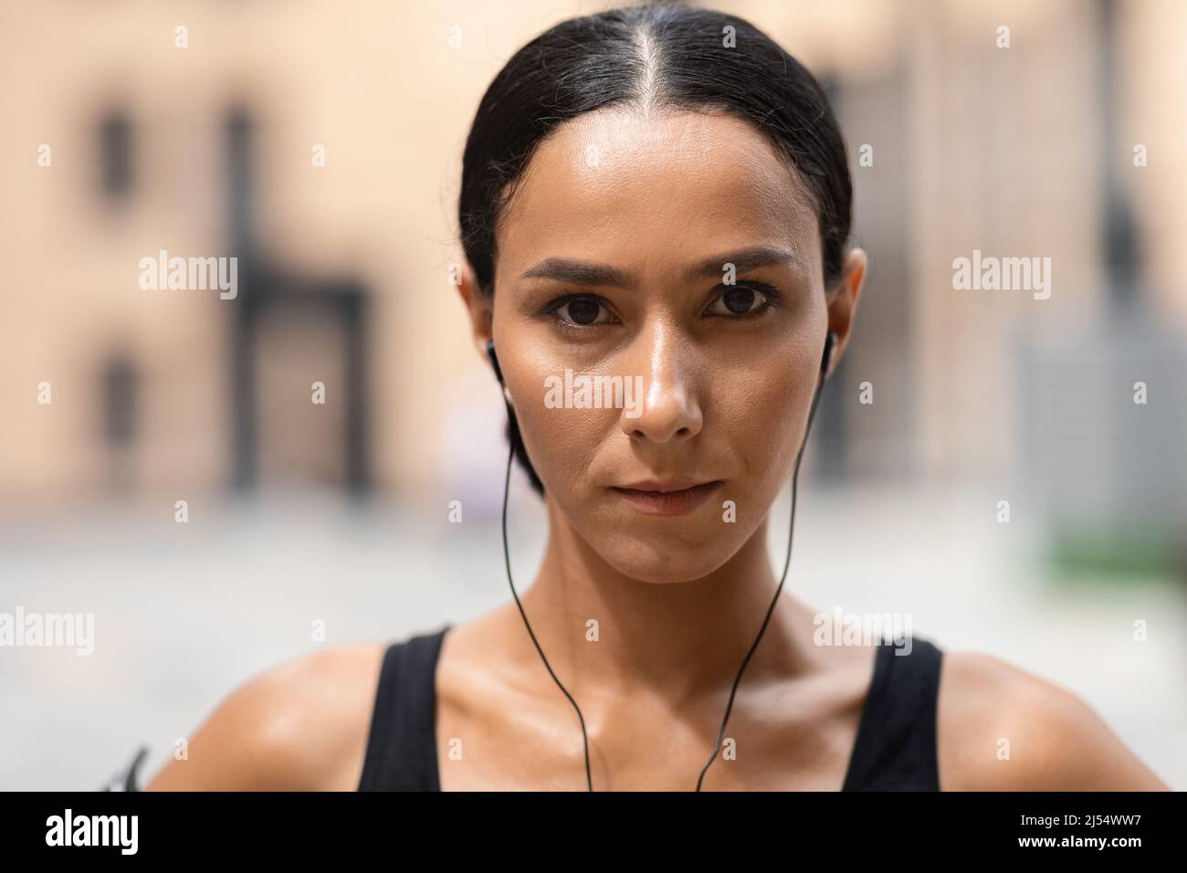 Una mujer atleta árabe morena milenaria segura en los auriculares mira la cámara sobre el fondo del edificio Foto de stock