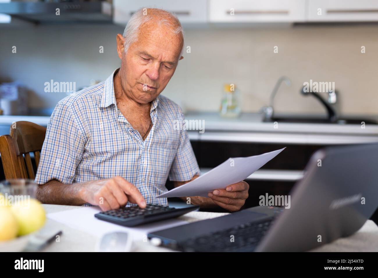 El hombre mayor calcula las ganancias y pérdidas del comercio en línea en la calculadora Foto de stock
