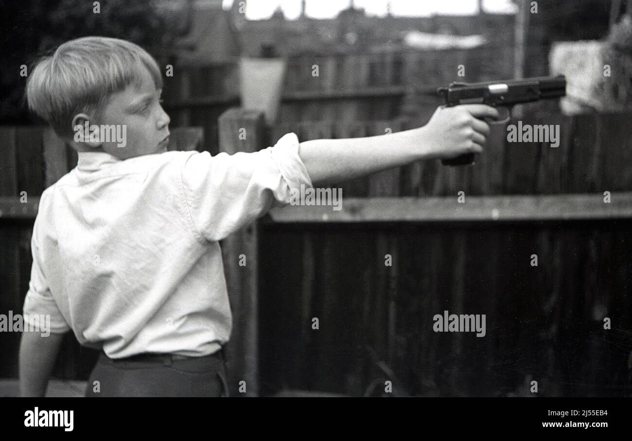 1950s, histórico, fuera en un patio trasero, niño sosteniendo una pistola de aire o pistola de aire, a la longitud de los brazos en una posición de tiro, Inglaterra, Reino Unido. Foto de stock
