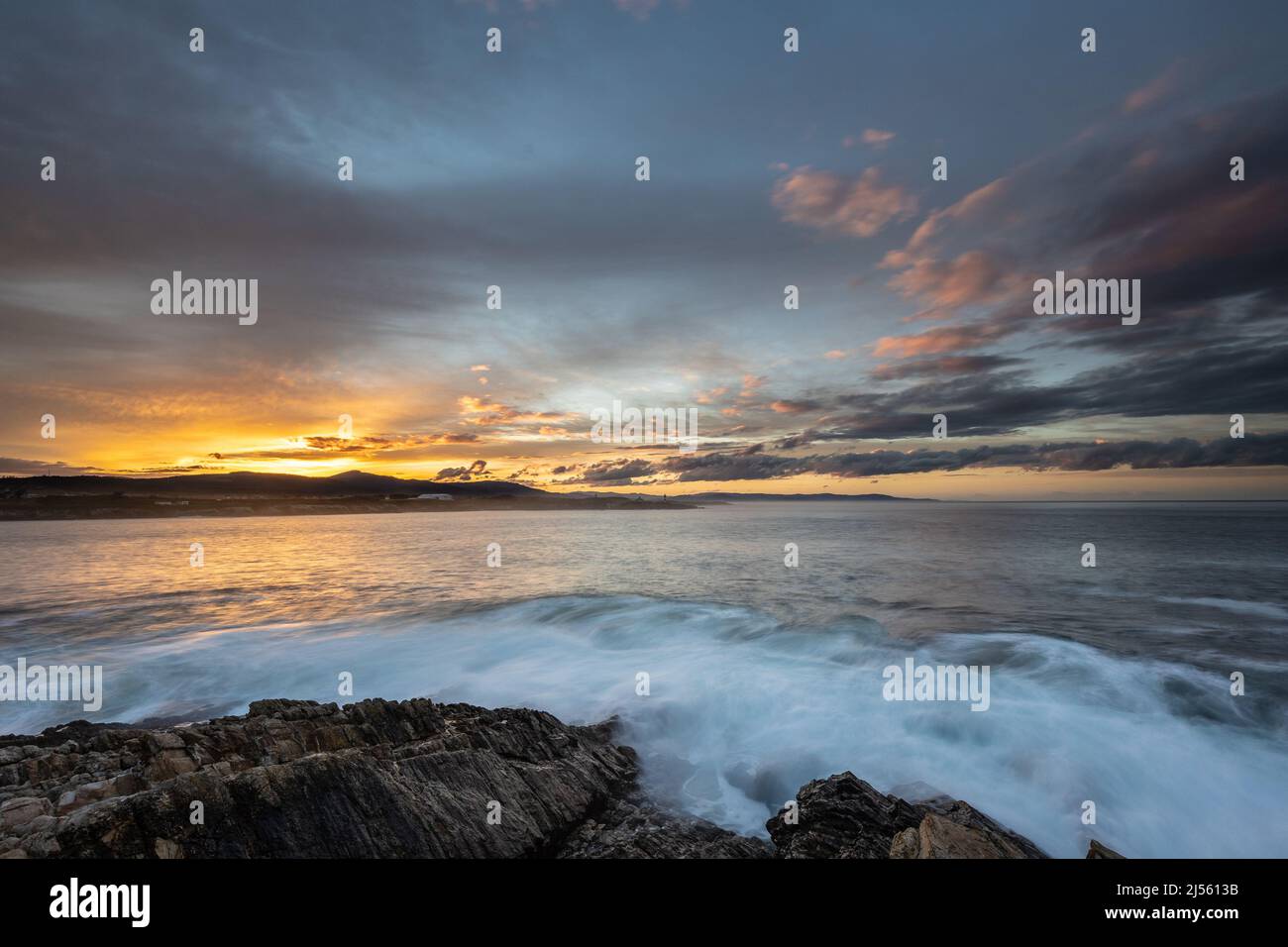 Espectacular y colorida puesta de sol en la costa de Asturias con un faro como protagonista Foto de stock