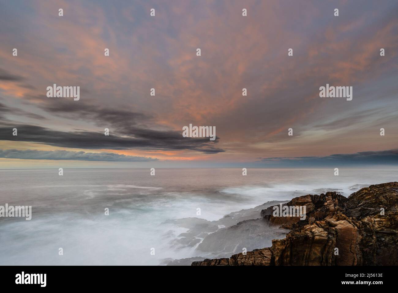 Espectacular y colorida puesta de sol en la costa de Asturias con un faro como protagonista Foto de stock