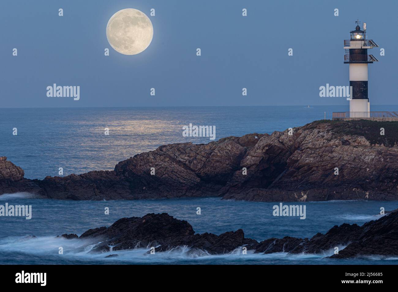¡Luna llena en la costa cántabra, con un faro y arcos naturales! Foto de stock