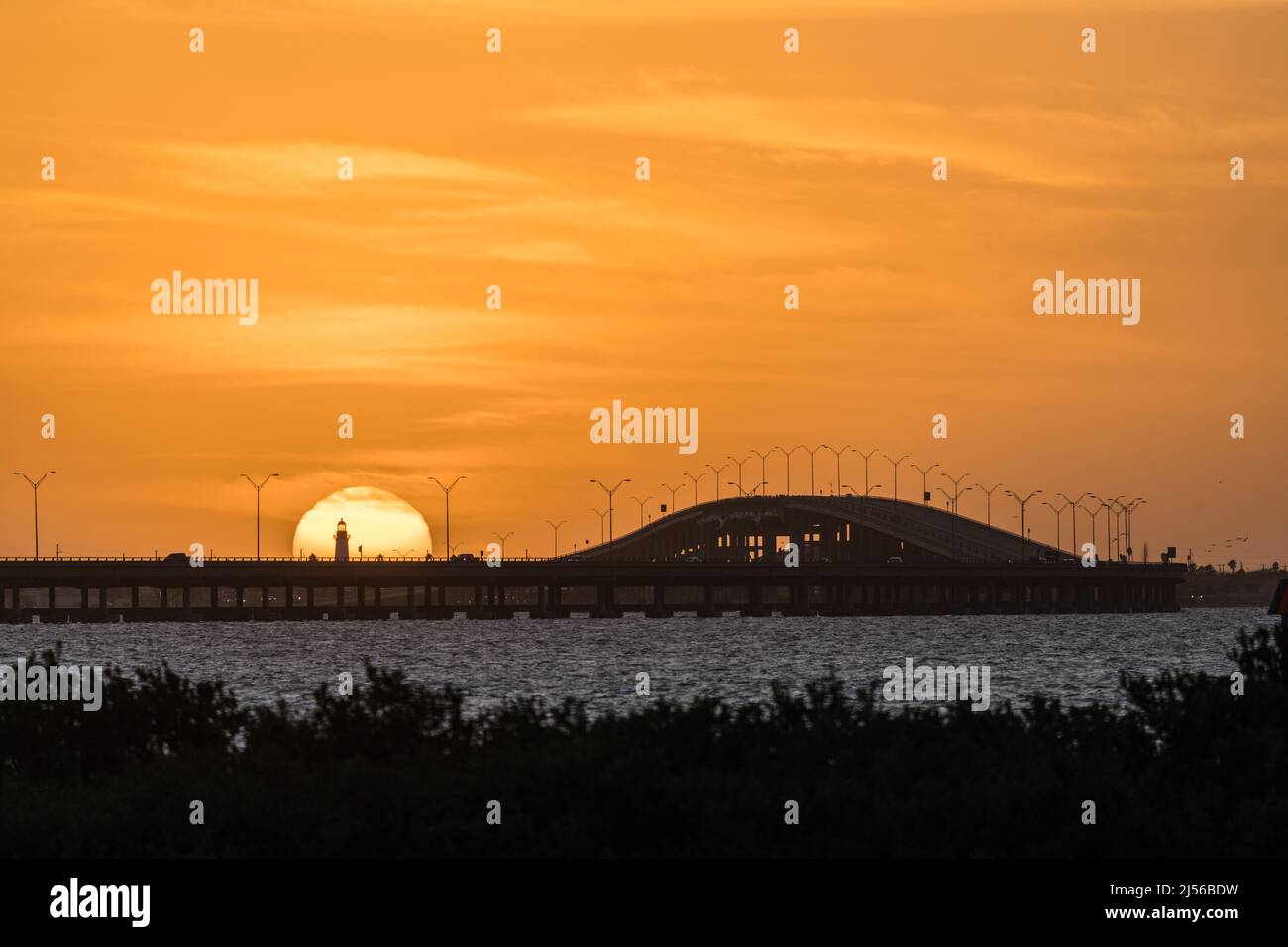 El faro de Port Isabel frente al sol poniente con el puente memorial Queen Isabella a la derecha. Texas. Visto al otro lado de la Laguna Madre f Foto de stock
