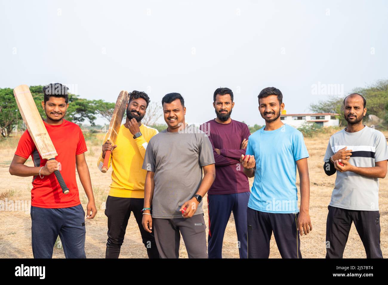 Concéntrese en el hombre con camiseta amarilla, el equipo de jugadores de cricket con bate y balón viniendo y de pie mirando la cámara en el campo - el conpet de la competición Foto de stock