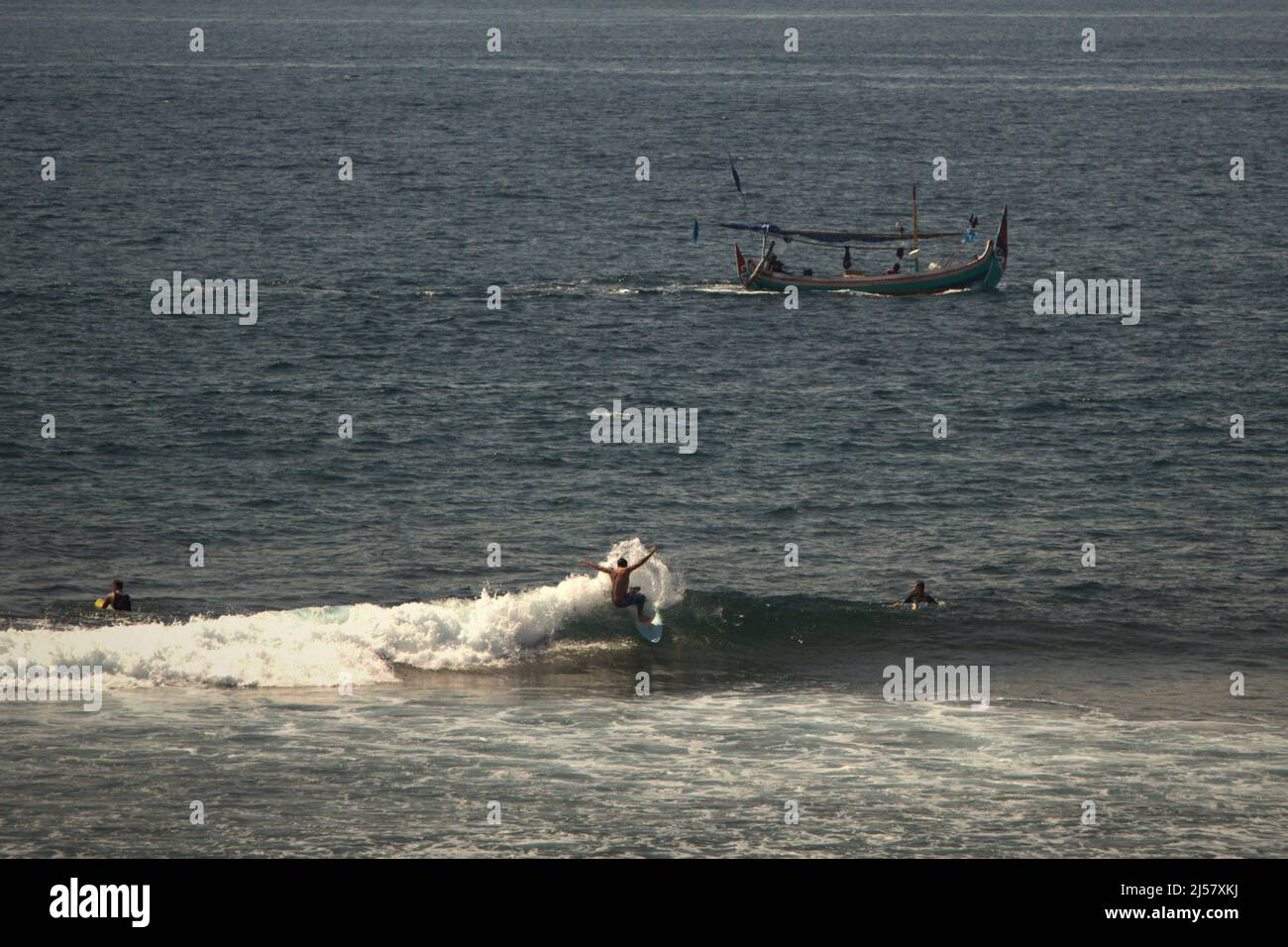 Un surfista montando una ola, en un fondo de un barco de pesca en la playa de Padang-padang en Labuan Sait, Kuta del Sur, Bali, Indonesia. Foto de stock