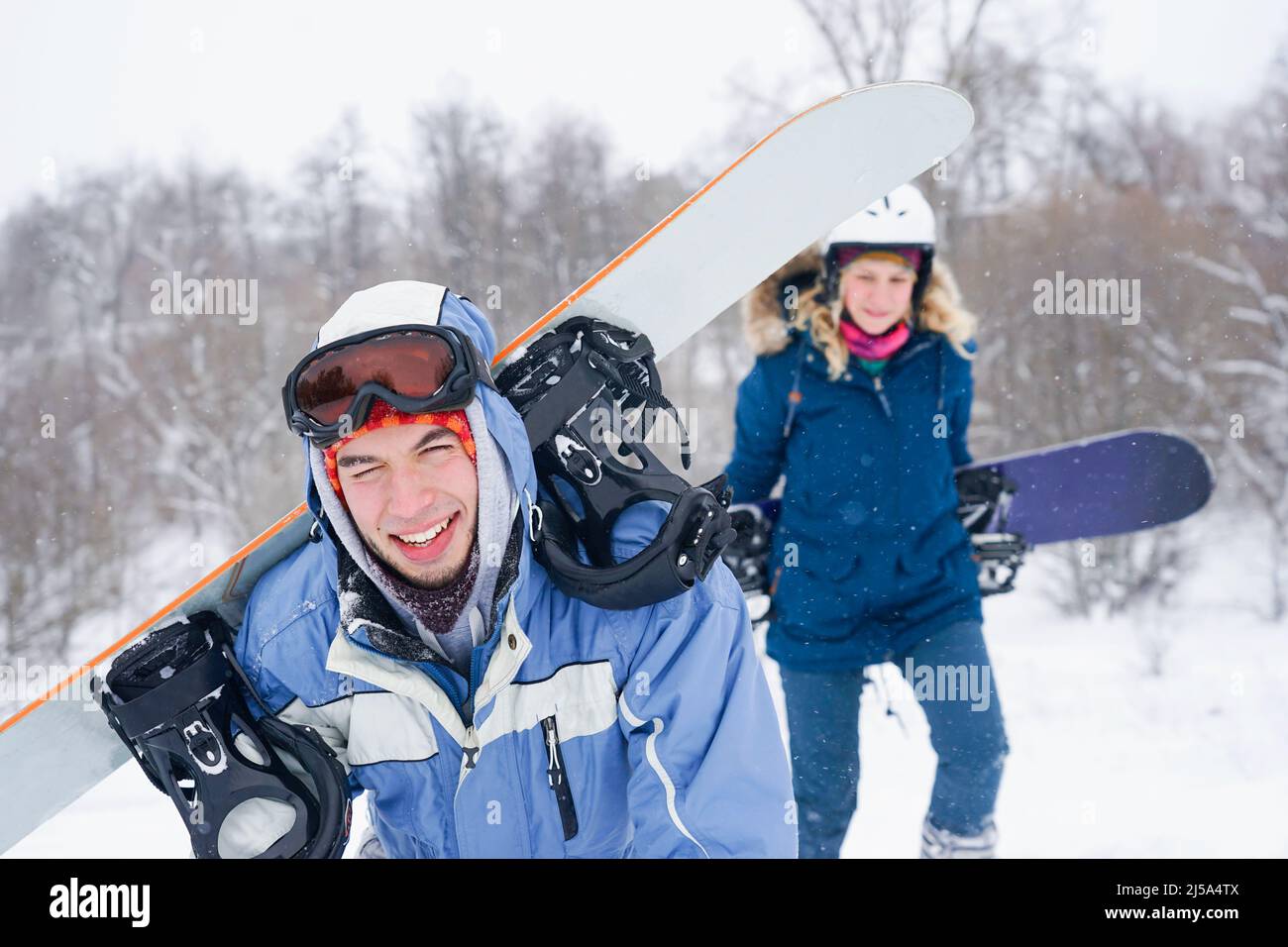 Un chico y una chica con ropa de snowboard caminan por la pista de esquí.  Tienen una tabla de snowboard. Vacaciones de invierno en las montañas  Fotografía de stock - Alamy