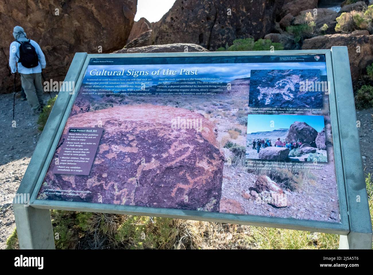 Petroglifo señal de información, Rings Loop sendero en la Reserva Nacional de Mojave. Un excursionista observa el arte rupestre antiguo en el estilo abstracto Curvilinear de Great Basin Foto de stock