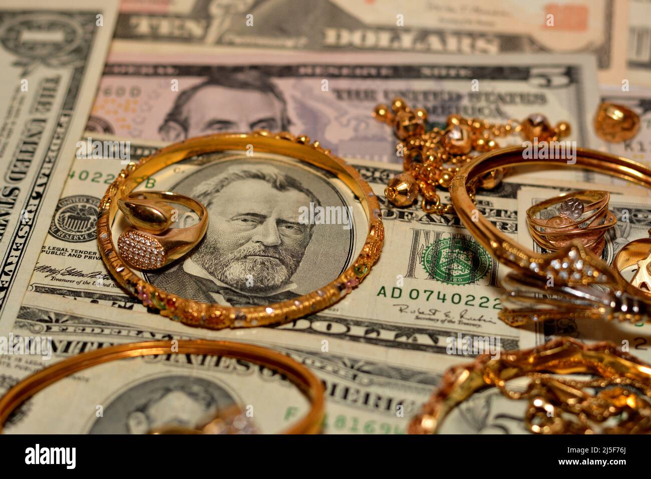 Un conjunto de accesorios de oro anillos, y pulseras en dólares americanos billetes dinero de diferentes valores, concepto de valor de oro, comprador de joyas, p Fotografía de stock -