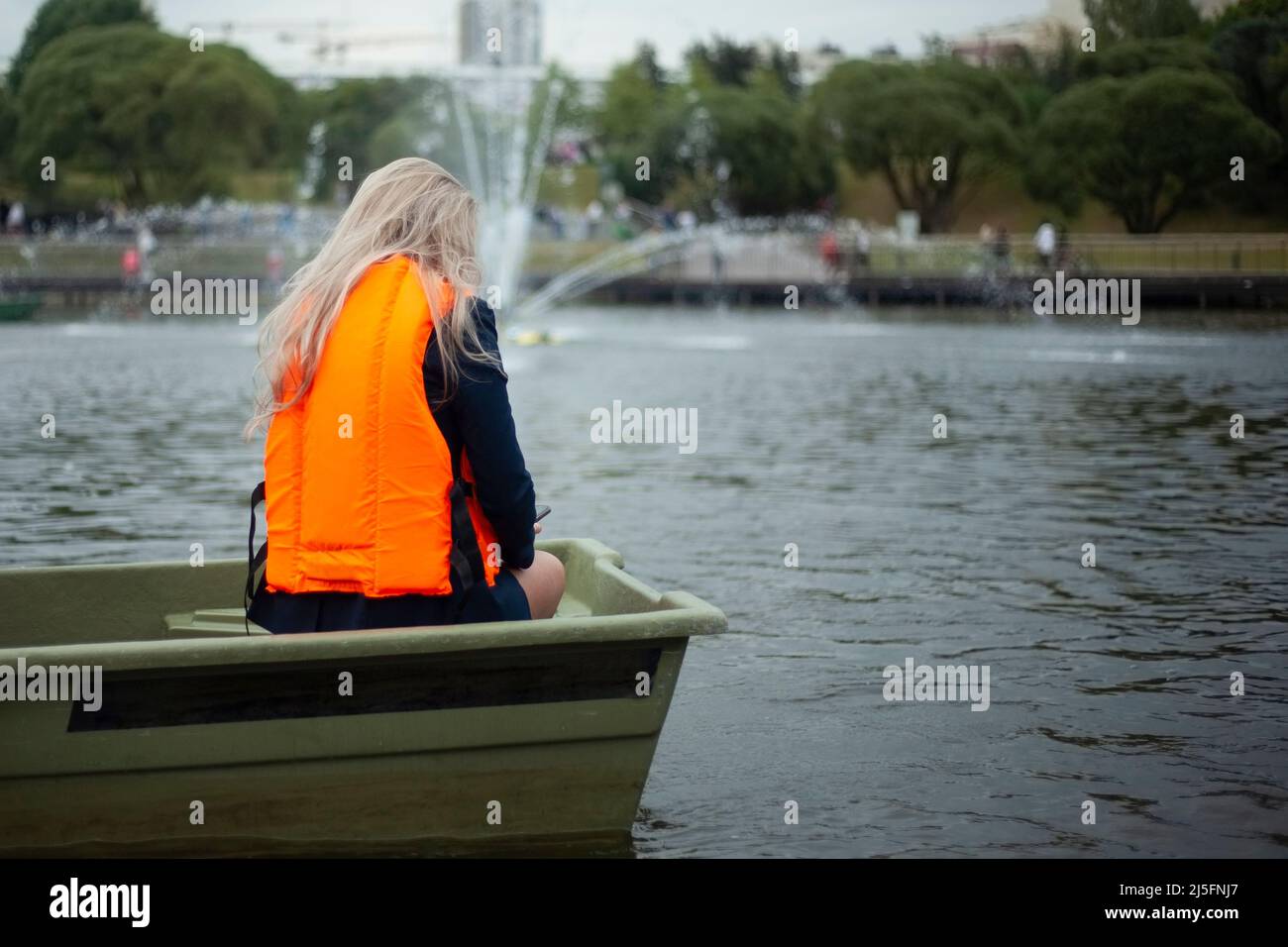 Una chica en un terreno en un barco. Mujeres en un chaleco de seguridad de agua naranja. Un hombre en el parque está navegando. Foto de stock