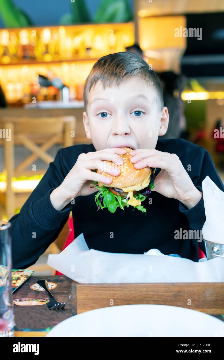 chico lindo rellenando una hamburguesa en un restaurante tratando de comerla Foto de stock