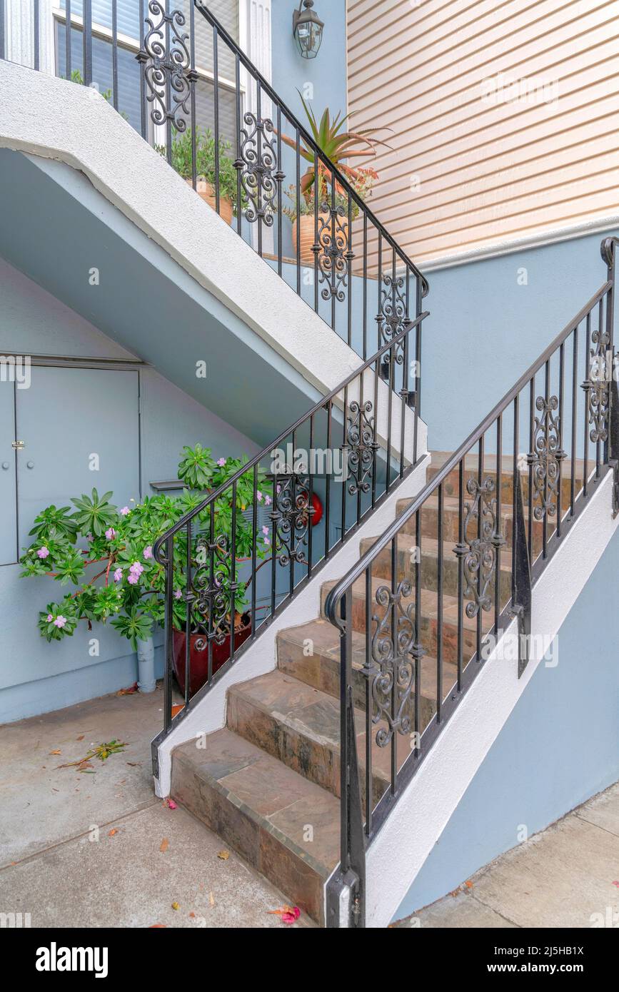 Escaleras fuera de la casa con plantas en macetas, barandilla de hierro  forjado, y escalones de baldosas de piedra. Exterior de una casa paredes de  color azul claro y paredes de madera