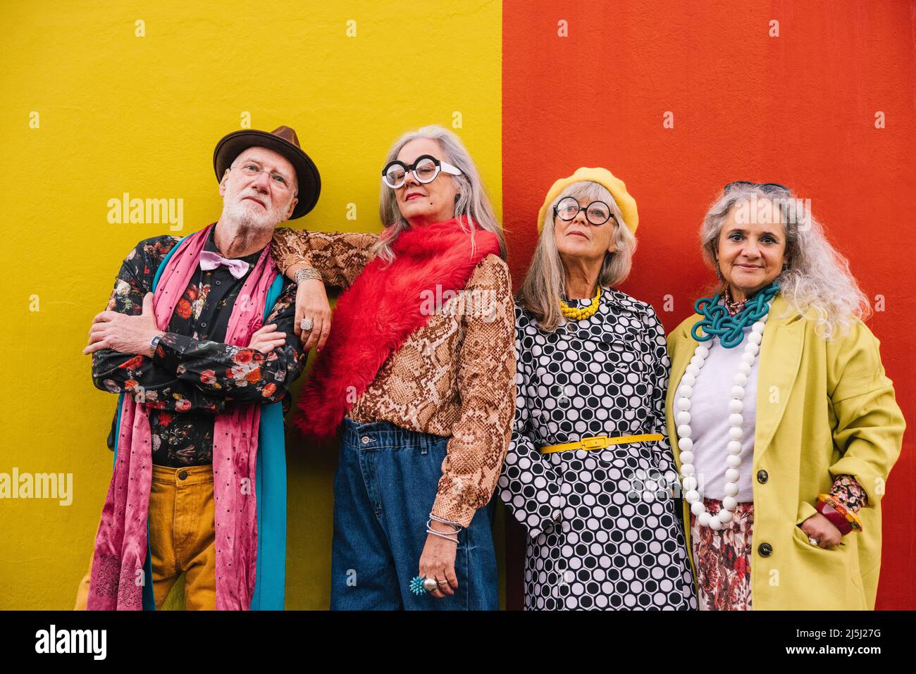 Gente anciana vibrante mirando la cámara mientras que parada junto contra una pared colorida. Grupo de cuatro personas mayores que se sienten confiados y usted Foto de stock