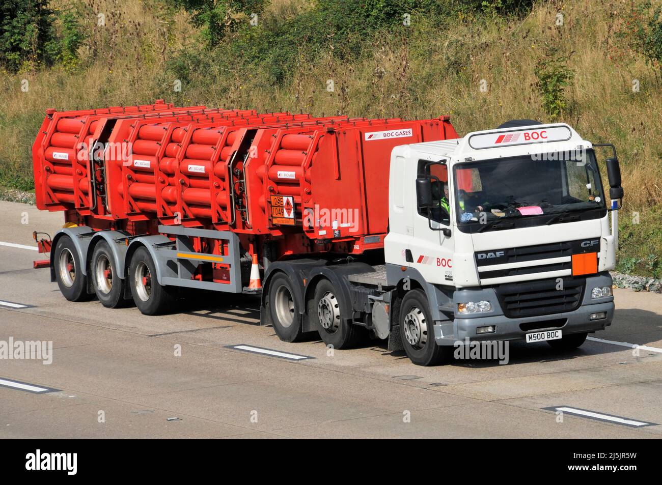 Vista lateral delantera Una empresa de gas BOC, camión DAF hgv y conductor con remolque articulado de cilindros rojos que contienen gases BOC que conducen por la autopista del Reino Unido Foto de stock